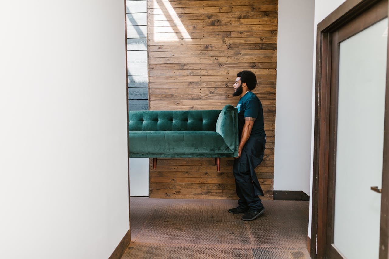 why-choose-us A mover carries a green sofa indoors, showcasing modern interior design and relocation services.